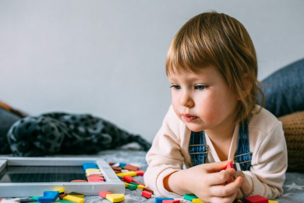 A small child plays at home an educational game with a multi-colored magnetic puzzle.