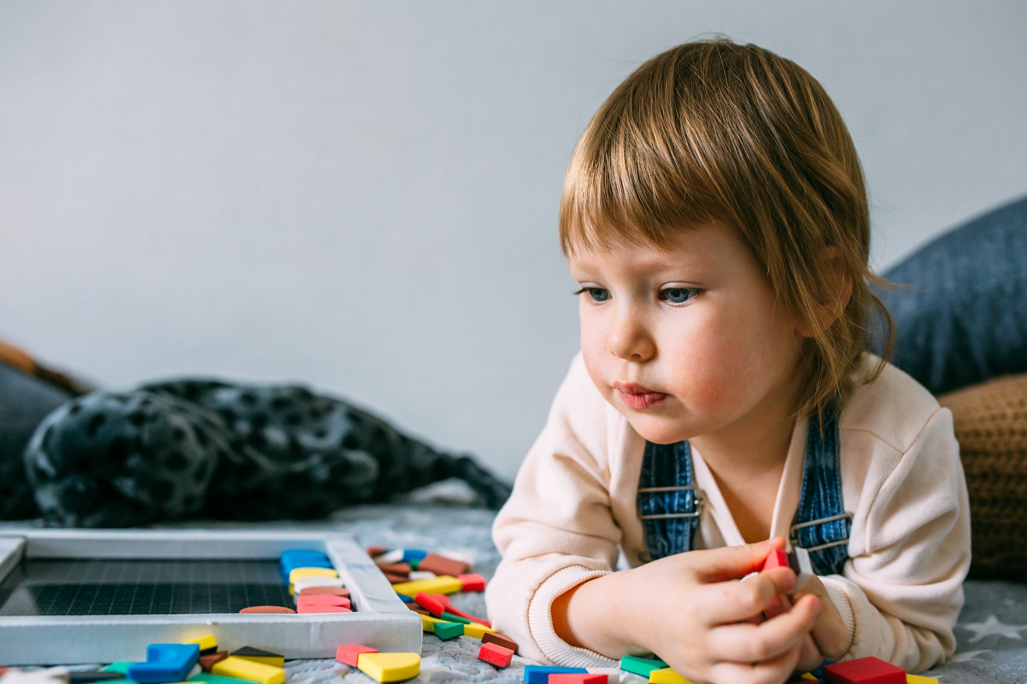 A small child plays at home an educational game with a multi-colored magnetic puzzle.