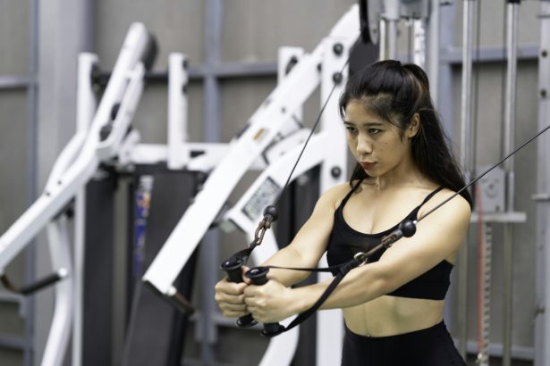 Young Asia lady exercise doing exercise-machine Cable Crossover fat burning workout in fitness class