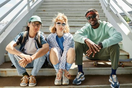 Young people wearing street style clothes outdoors while sitting on stairs