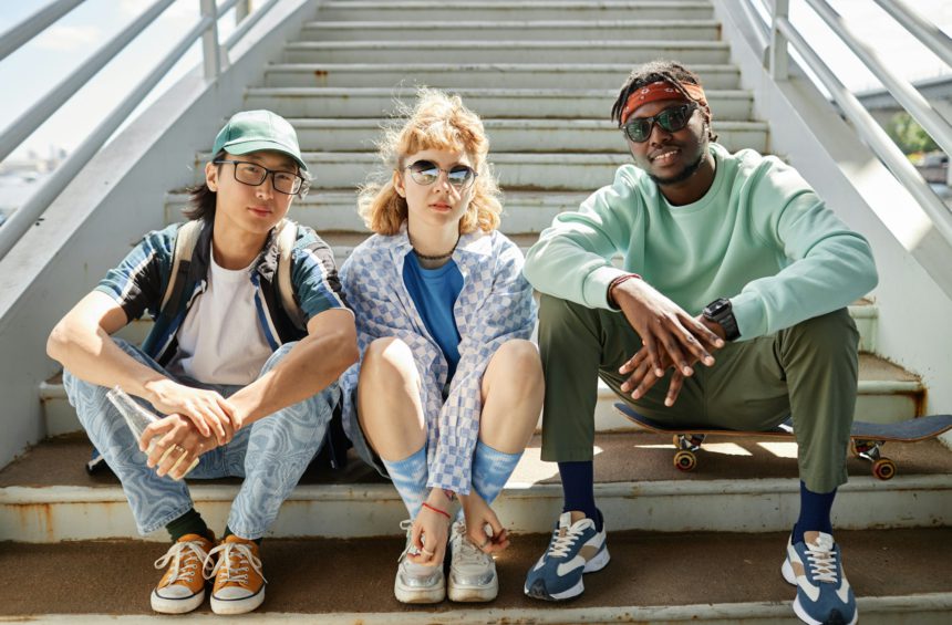 Young people wearing street style clothes outdoors while sitting on stairs